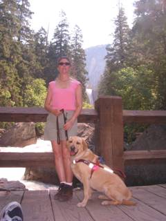 Janice standing with her guide dog, Liza, on a bridge overlooking Vernal Falls in Yosemite