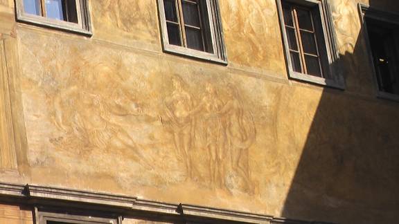Fresco on outside wall of building. 3 scantly clad women serving a queen. 