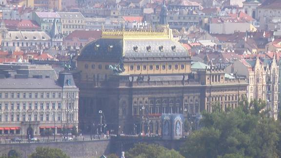 4 story building with a partially rounded roof top. Windows stick out of the roof top. On the very top sets gold railing and wall like a crown.