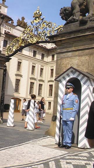 Uniformed guard standing by palace gate. The rott iron arch over the top of the gate is trimmed in gold with a gold crown on the very top.